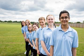 Row of school girls lined up behind each other on the playing field. 