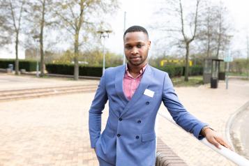 man wearing a suit standing in an open park leaning on a fence